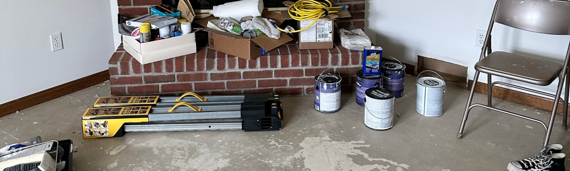 A traditional brick fireplace with various home improvement tools and extension cords piled up around it.