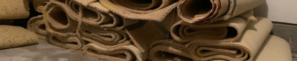 A towering pile of rolled-up carpet strips and carpet padding piled inside of a garage.